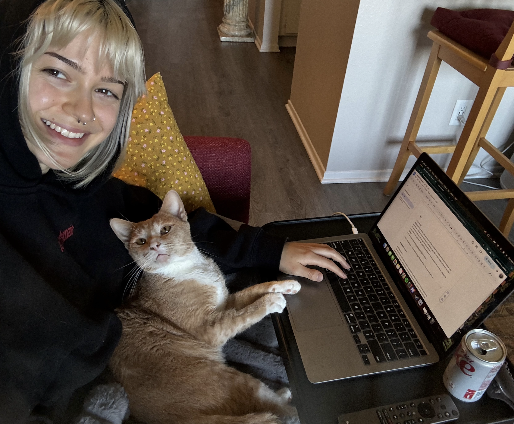 Emmy sitting with Moose, her orange cat, in her lap while working at her laptop.